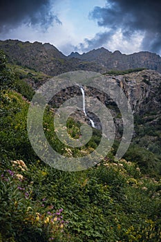 An incredible view of a majestic Shdugra waterfall in the distance, high in the Caucasus Mountains, rocky slopes, a rushing stream