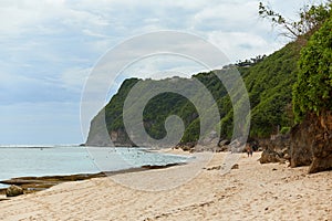 An incredibly beautiful deserted tropical beach under a cliff with clear, clean ocean water on the popular tourist island of Bali