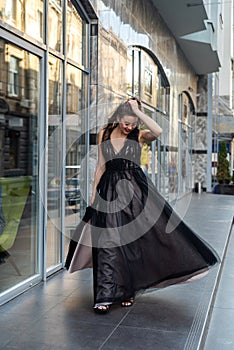 Incredibly beautiful full-length woman posing among the city in an amazing black evening dress