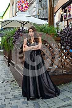 Incredibly beautiful full-length woman posing among the city in an amazing black evening dress
