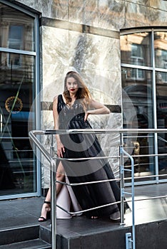 incredibly beautiful full-length woman posing among the city in an amazing black evening dress.