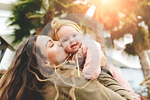 Incredibly beautiful mother holding in her arms her daughter and kissing outside. Fashionable stylish look