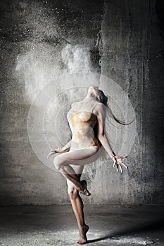 Incredibly beautiful pose of a dancer with flying flour on a gray background.