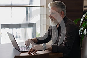 an incredibly beautiful and stylish gray-haired man of fifty years old working with a laptop