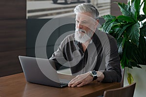 an incredibly beautiful and stylish gray-haired man of fifty years old working with a laptop