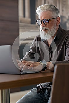 an incredibly beautiful and stylish gray-haired man of fifty years old working with a laptop