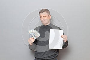 Incredulous man is holding US dollars and white blank paper sheet photo