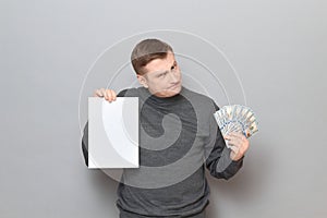 Incredulous man is holding US dollars and white blank paper sheet photo