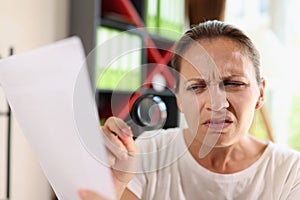 Incredulous middle age woman looking on document trough magnifying glass close-up.