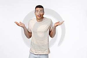 Indecisive handsome hispanic man with short haircut, wear t-shirt, shrugging with arms spread sideways look worried and
