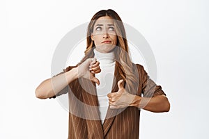 Indecisive middle aged corporate woman weighing decision, showing like dislike gesture, thumbs up and thumbs down