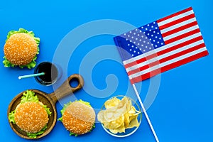 Independence Day of America concept with flag, burgers, chips and drink on blue background top view