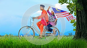 Independence Day concept - happy young local boy riding old bicycle at paddy field holding a Malaysian flag photo