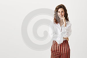 Independent attractive woman with successful look, standing in fashionable outfit, smiling while holding index finger on