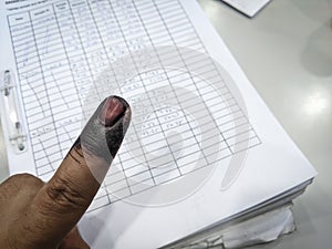 Index finger with indelible ink stain after voting in election with record form background.
