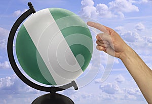 The index finger of a male hand points to a globe with a colored national state flag nigeria