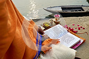 India. Varanasi Benares Uttar Pradesh. A man reading sacred texts of hinduism and praying by the river Ganges at sunrise