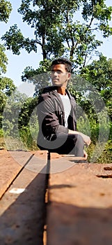 A Indian adult male sitting on the iron plats, he wears a black jacket and trouser.