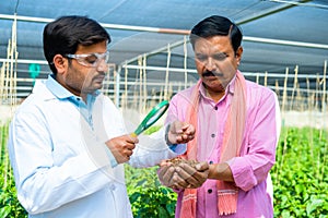 Indian agro scientist checking soil from famer hand at greenhouse using magnifying glass - concept of biotechnology