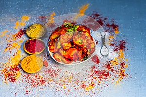 Indian appetizer dish i.e.Teekha Laal Batata or Spicy potato with all its ingredients and spices on a sliver wooden surface.This d