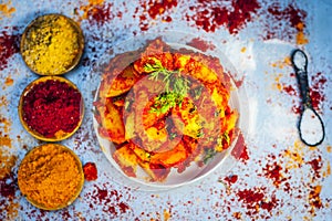 Indian appetizer dish i.e.Teekha Laal Batata or Spicy potato with all its ingredients and spices on a sliver wooden surface.This d