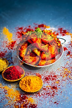 Indian appetizer dish i.e.Teekha Laal Batata or Spicy potato with all its ingredients and spices on a sliver wooden surface.This d