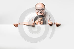 Indian asian cute little girl pointing at blank white board with grandpa or grandfather