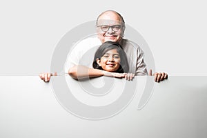 Indian asian cute little girl pointing at blank white board with grandpa or grandfather