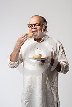 Indian asian Senior man or old man eating Samosa snack