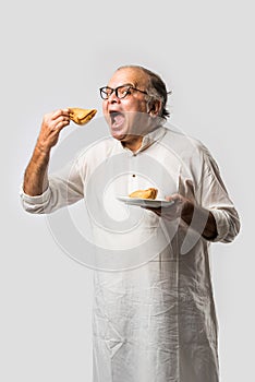 Indian asian Senior man or old man eating Samosa snack