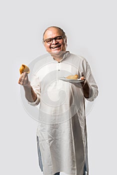 Indian asian Senior man or old man eating Samosa snack