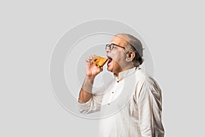 Indian asian Senior man or old man eating Samosa snack