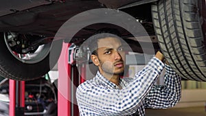 Indian auto mechanic working under car on hydraulic lift in garage