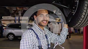 Indian auto mechanic working under car on hydraulic lift in garage