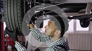 Indian auto mechanic working under car on hydraulic lift in garage