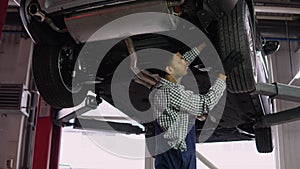 Indian auto mechanic working under car on hydraulic lift in garage