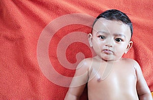 An indian baby boy lying on orange towel after being oil massaged and looking at the camera