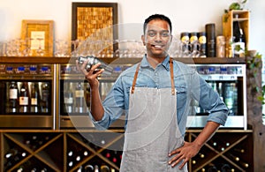 Indian barman in apron with cocktail shaker at bar