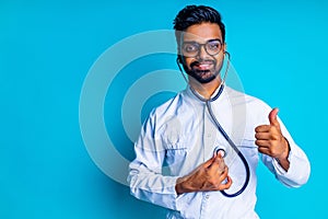 indian bearded cardiologist man with eyes glasses in white medical coat with stethoscope in blue studio background