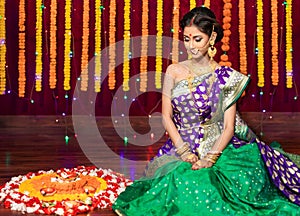 Indian Beautiful young girl wearing traditional sari making Flower rangoli for diwali or onam or Pongal Festival,Studio shot with