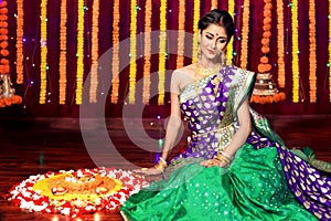 Indian Beautiful young girl wearing traditional sari making Flower rangoli for diwali or onam or Pongal Festival,Studio shot with