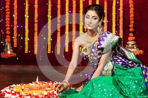 Indian Beautiful young girl wearing traditional sari making Flower rangoli for diwali or onam or Pongal Festival,Studio shot with