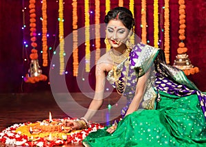 Indian Beautiful young girl wearing traditional sari making Flower rangoli for diwali or onam or Pongal Festival,Studio shot with