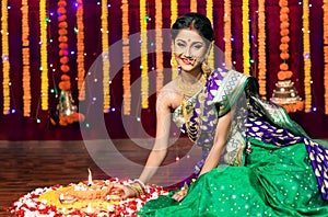 Indian Beautiful young girl wearing traditional sari making Flower rangoli for diwali or onam or Pongal Festival,Studio shot with