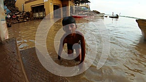 Indian boy comes to surface of dirty water flood holy river Ganges piles of whirewood on boats and stairs Manikarnika Ghat place o