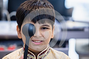 Indian boy examining eyesight checkup vision farsightedness examines ophthalmological hospital. doctor using occluder for eye