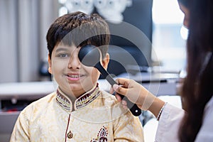 Indian boy examining eyesight checkup vision farsightedness examines ophthalmological hospital. doctor using occluder for eye photo