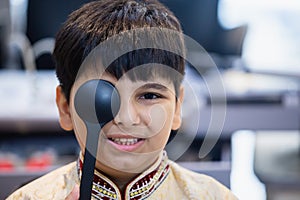 Indian boy examining eyesight checkup vision farsightedness examines ophthalmological hospital. doctor using occluder for eye photo