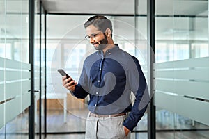 Indian business man employee using mobile phone standing in office.