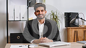 Indian business man sitting at office workplace desk closing laptop pc after finishing remote work